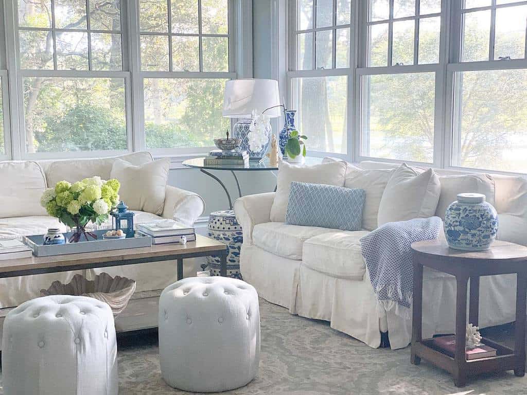 Elegant sunroom with white sofas, blue accents, floral decor, and soft natural lighting.