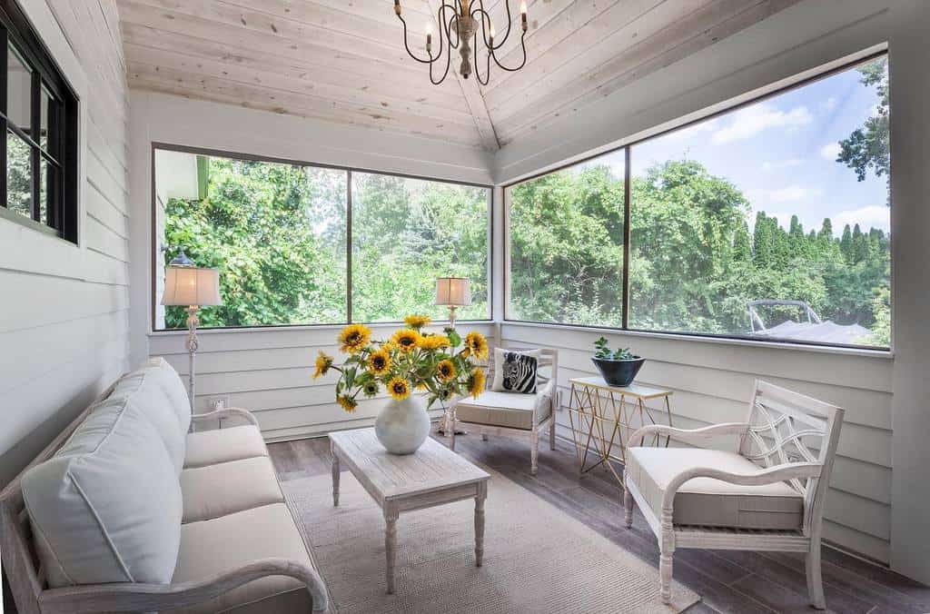 Bright sunroom with white furniture, wooden ceiling, sunflower centerpiece, and cozy decor.