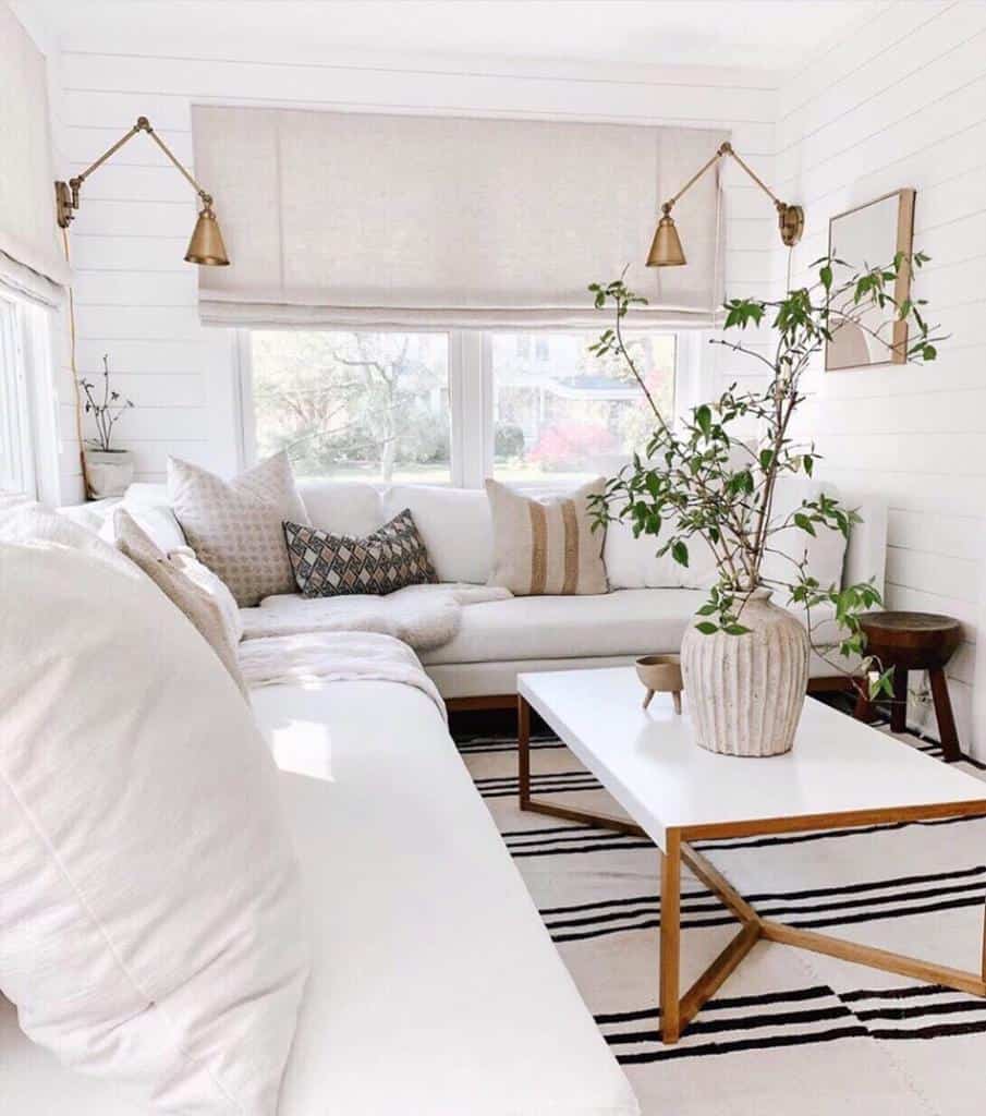 Minimalist sunroom with white sectional sofa, striped rug, modern coffee table, and potted plant.