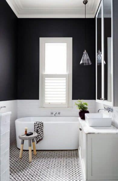 Elegant black and white bathroom with freestanding tub, patterned floor tiles, and pendant light.