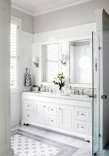 Elegant white bathroom with large mirror, floral arrangement, and patterned white tile floor