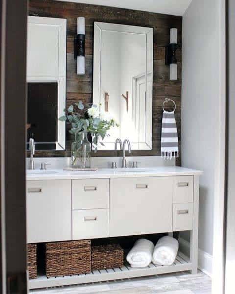 Rustic white bathroom vanity with twin mirrors, wicker baskets, towels, and a vase with flowers