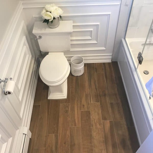 Bathroom with white wainscoting, wood-look tile floor, and traditional toilet.