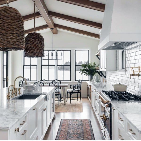 Two wicker ceiling lamps hang above a kitchen island, with a marble countertop, white cabinetry, and natural light coming through large windows