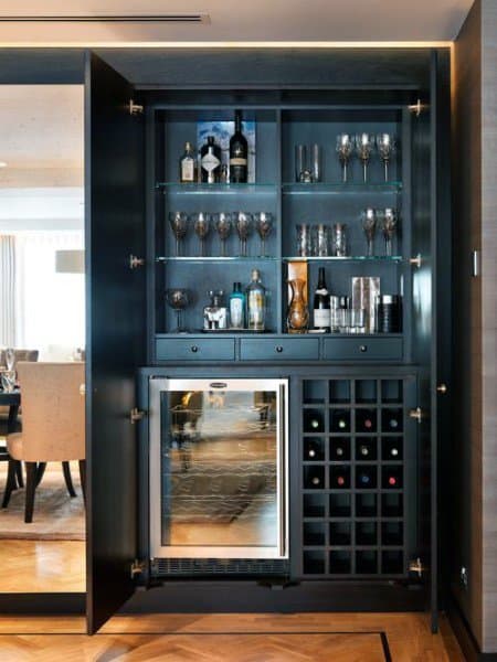 Elegant mini bar with glass shelves, wine fridge, bottle storage, and dark cabinetry.