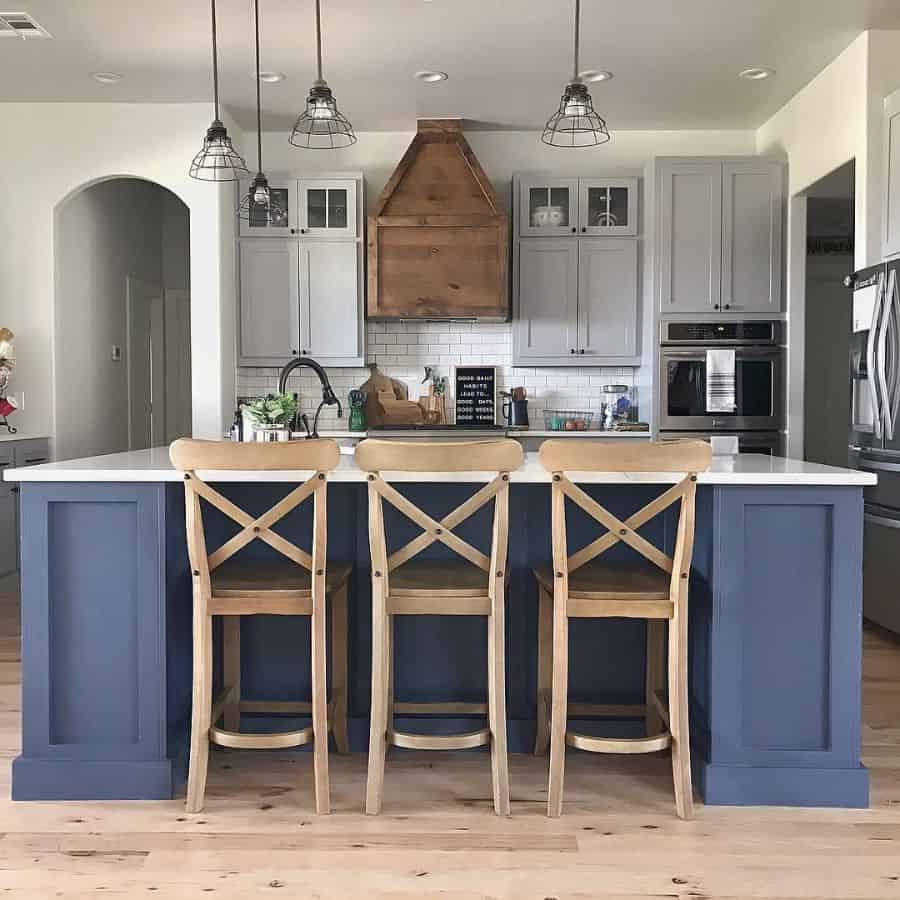 Modern farmhouse kitchen with blue island wooden barstools rustic wood hood and pendant lighting.