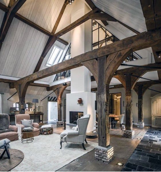 Spacious rustic living room with exposed wooden beams, large windows, a white fireplace, and a cozy seating area