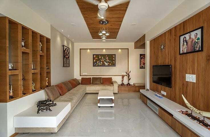 Modern living room featuring a beige sectional, brown wall art, wooden shelves, ceiling fan, and mounted TV