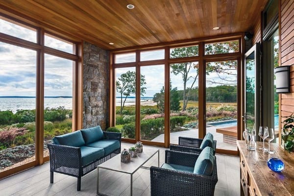 unroom with wood ceiling, stone wall, blue seating, glass windows, and waterfront view.