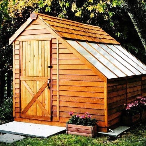 Wooden barn-style shed with slanted roof and side skylight, nestled in a garden.