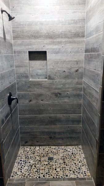 Rustic shower with wooden plank walls, pebble floor, and a built-in shelf