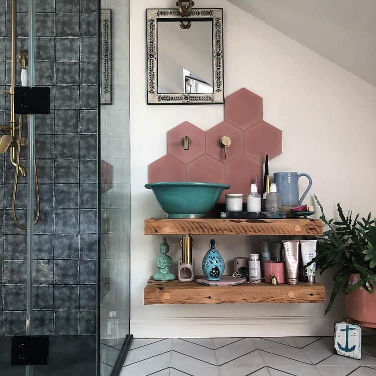 Modern bathroom with teal sink, pink hexagon tiles, and wooden shelves for storage.