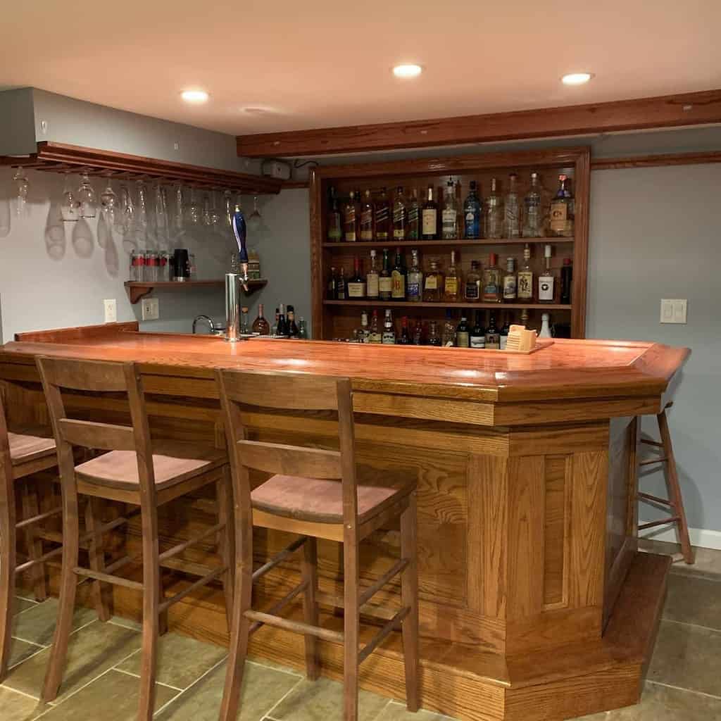 A cozy wooden wet bar with a polished countertop, bar stools, and shelves stocked with bottles.