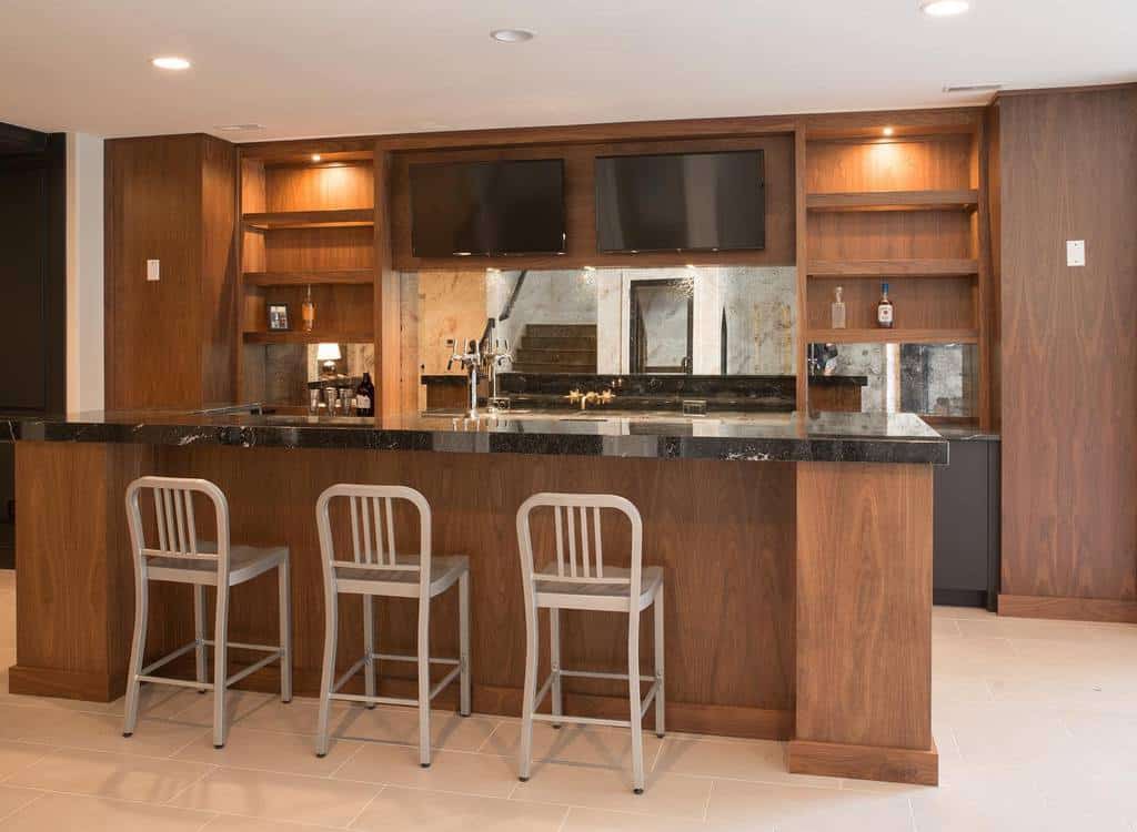 A sleek wooden wet bar with a black countertop, built-in shelves, and modern bar stools.