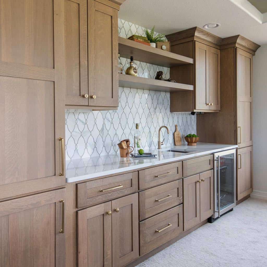 A stylish wood wet bar with gold accents, white countertops, and open shelving.