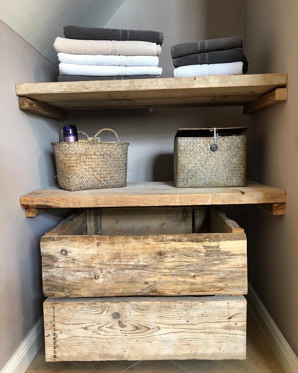 Rustic wooden bathroom shelves with folded towels, wicker baskets, and wooden storage drawers.