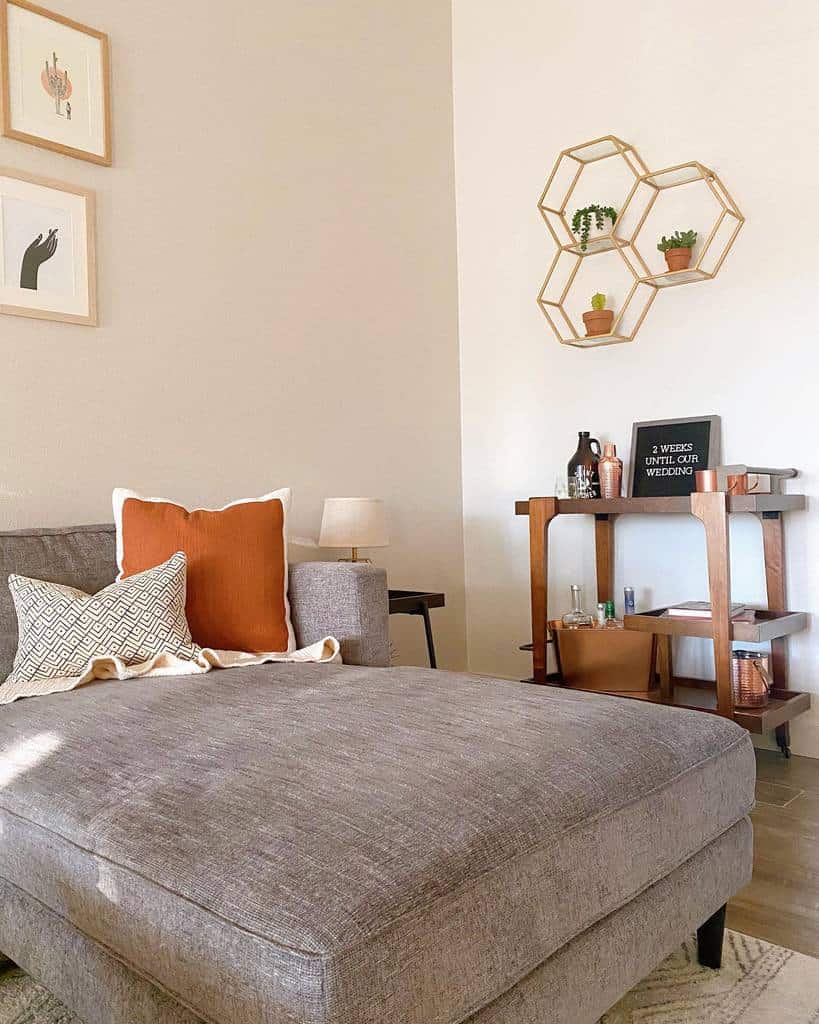 Wooden bar cart with copper accents in a cozy living room featuring geometric wall shelves and decor.