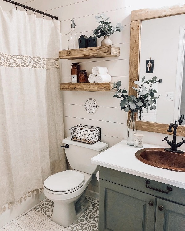 Cozy farmhouse bathroom with a white shower curtain, wooden shelves, potted plant, and decor above toilet and sink