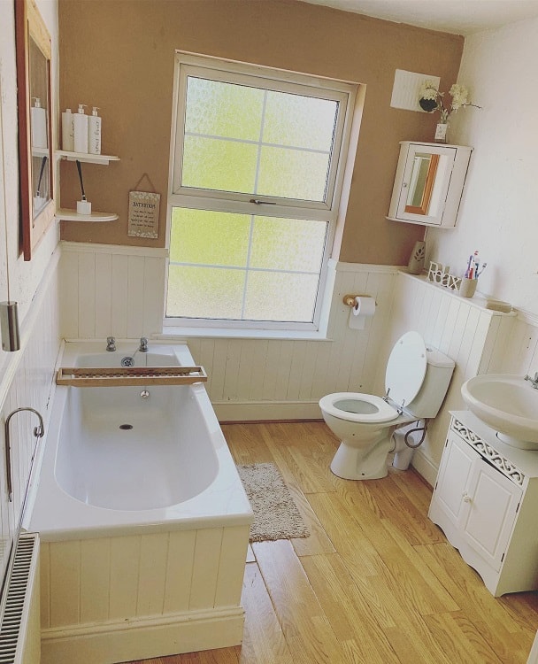 Cozy farmhouse bathroom with white bathtub, wooden flooring, and frosted window.