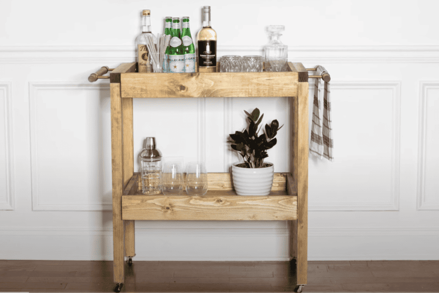 Wooden bar cart with bottles, glassware, and a potted plant, featuring a DIY rustic design.