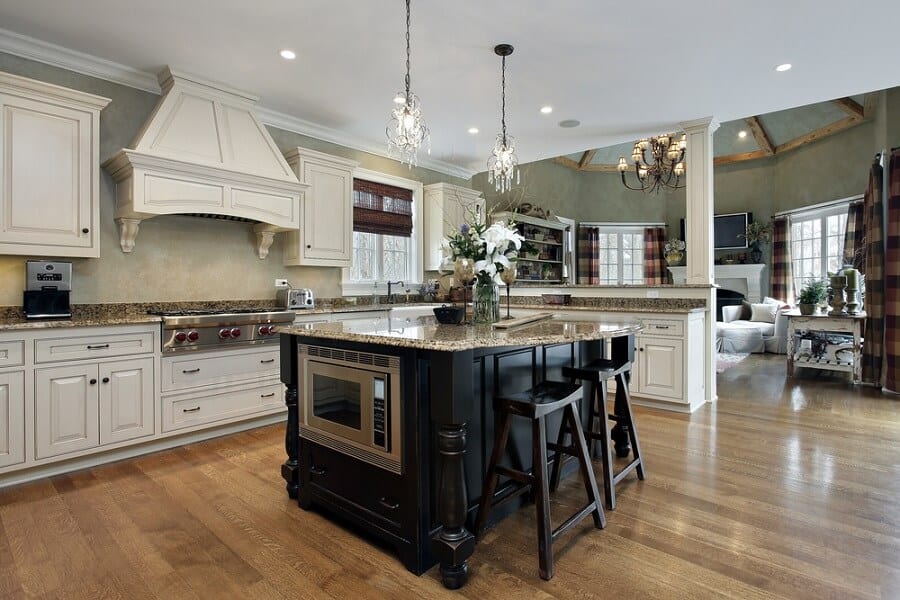 Spacious kitchen with wooden floors, white cabinets, and a large island featuring barstools and elegant hanging lights